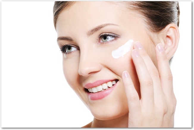Pretty smiling female applying cosmetic cream on face